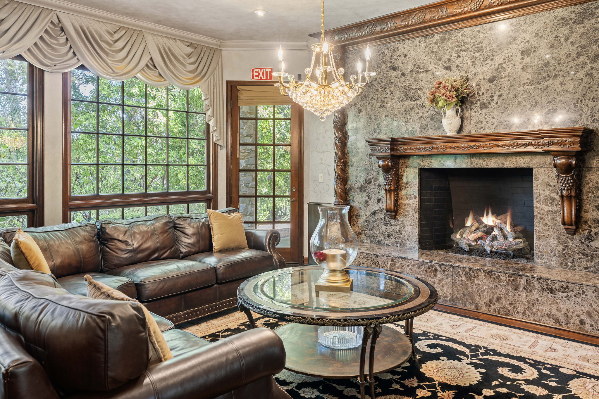 Common lounge with leather seating around a marble fireplace beneath a crystal chandelier
